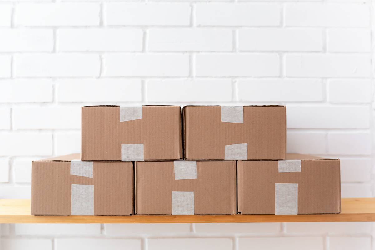 Plain brown cartons stacked on a wooden shelf against a white brick wall