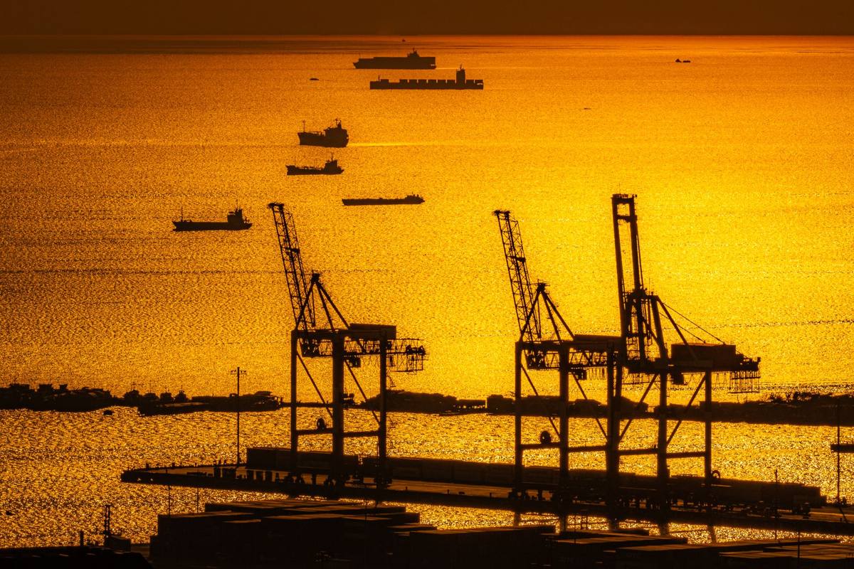 Silhouettes of port cranes and ships on golden water